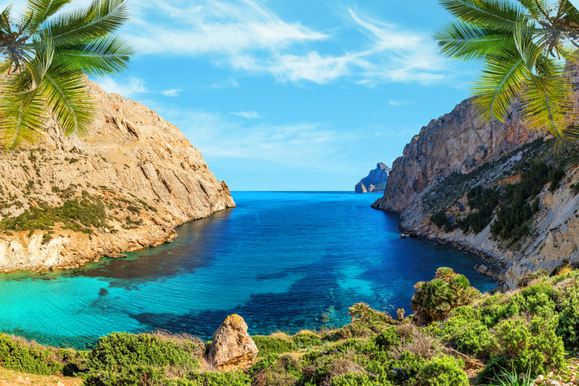 Mallorca Atemberaubende Aussicht auf eine türkisfarbene Bucht auf Mallorca, eingerahmt von hohen Felsklippen und tropischen Palmen im Vordergrund