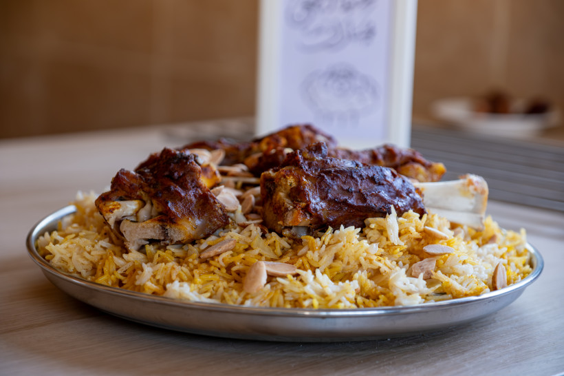 Ägypten - Sharm el Sheikh Ein orientalisches Gericht mit geschmortem Lammfleisch auf einem großzügigen Bett aus gelbem Safranreis, garniert mit gerösteten Mandelsplittern. Serviert wird das Gericht auf einem runden Metalltablett auf einem hellen Holztisch. Im Hintergrund ist unsch