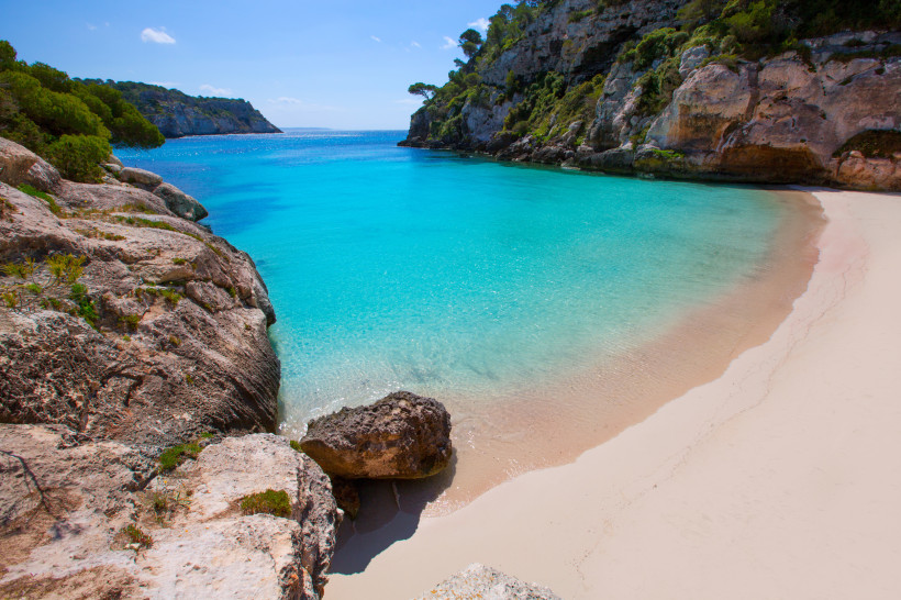 Menorca - Cala Macarelleta Cala Macarelleta auf Menorca: kleine Badebucht mit kristallklarem Wasser, Felsen und grüner Vegetation. Urlauber schwimmen und entspannen am Strand.