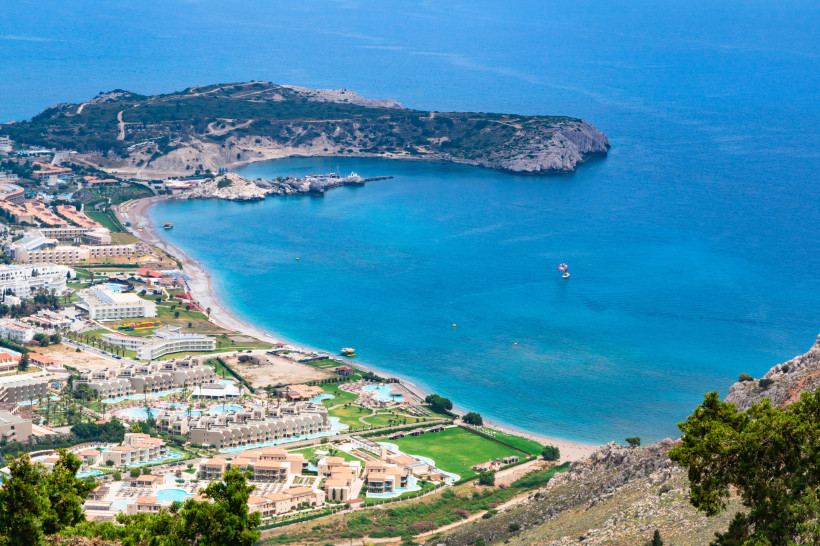 Panoramablick auf eine große Bucht auf Rhodos mit türkisblauem Meer, Sandstrand, Hotelanlagen, Pools und felsiger Halbinsel im Hintergrund