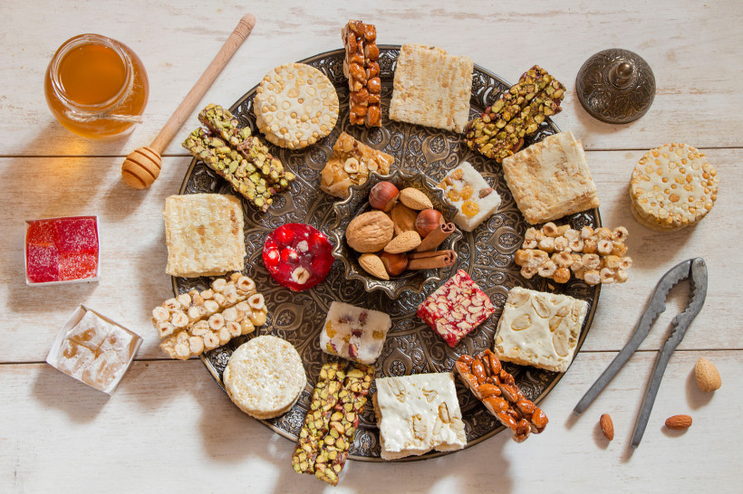 Ägypten - Makadi Bay Silberfarbener Servierteller mit orientalischen Süßigkeiten wie Nussriegel, Sesamgebäck, Nougat und türkischem Honig. In der Mitte eine Schale mit Zimtstangen und Nüssen.