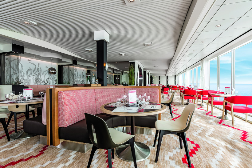 Innenansicht des Restaurants GOSCH Sylt auf der Mein Schiff 6 mit gedeckten Tischen und Fensterfront