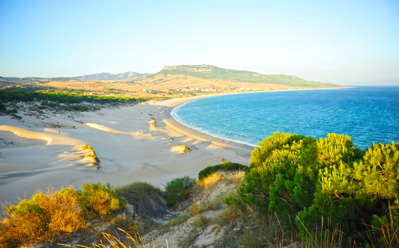 Blick auf die Playa de Bolonia mit Sanddünen, Strandbogen und blauem Meer vor einer Hügellandschaft
