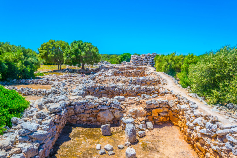 Steinruinen der prähistorischen Siedlung Capocorb Vell mit Trockenmauern und Weg unter blauem Himmel