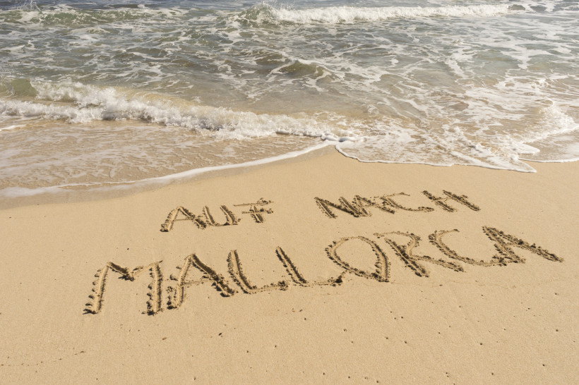 Mallorca Handschriftlicher Schriftzug 'Auf nach Mallorca' im Sand am Strand, mit Wellen im Hintergrund