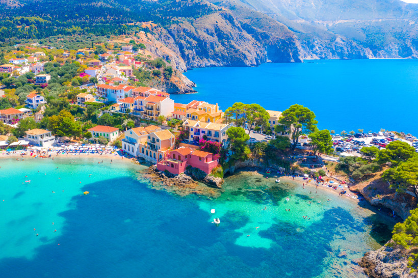 Küstenort auf Kefalonia mit bunten Häusern am Strand und türkisblauem Meer vor steilen Felsen