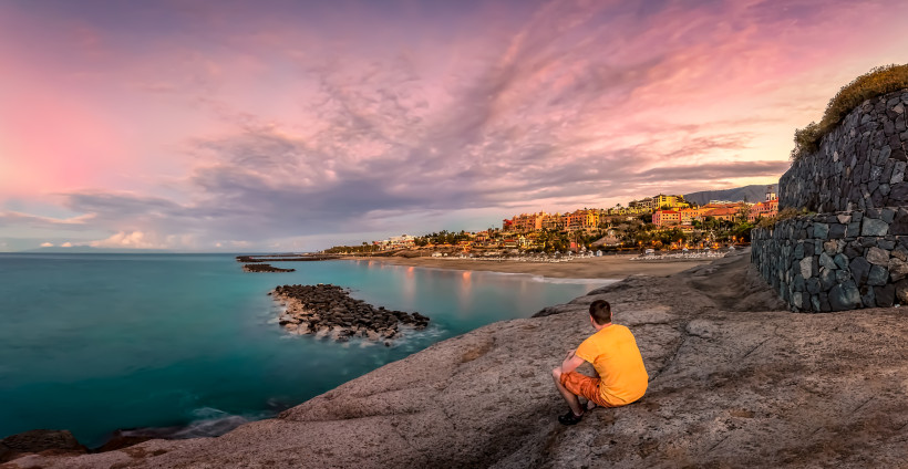 Sonnenuntergang an der Costa Adeje – Traumhafte Abendstimmung auf Teneriffa Sonnenuntergang an der Costa Adeje auf Teneriffa mit Blick auf die Küste und einen sitzenden Reisenden auf den Felsen.