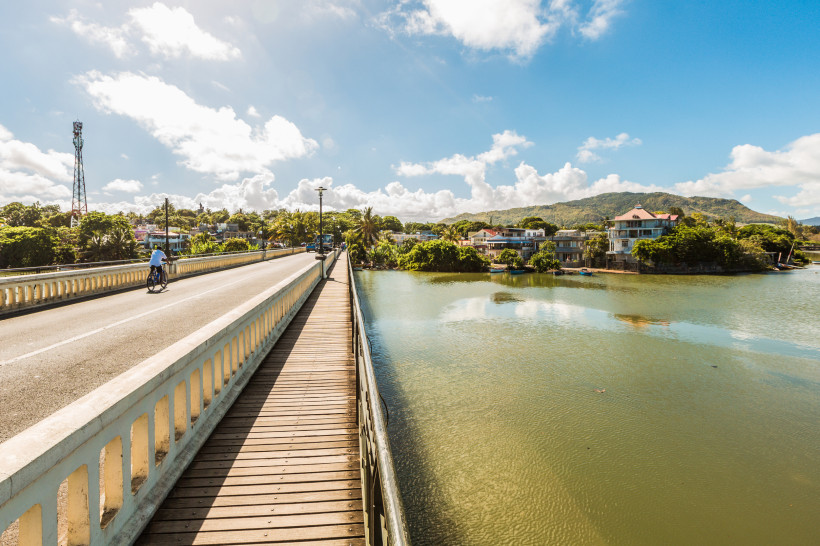 Brücke über den Fluss in Mahébourg mit Blick auf Kolonialhäuser, Palmen und die umliegenden Berge auf Mauritius