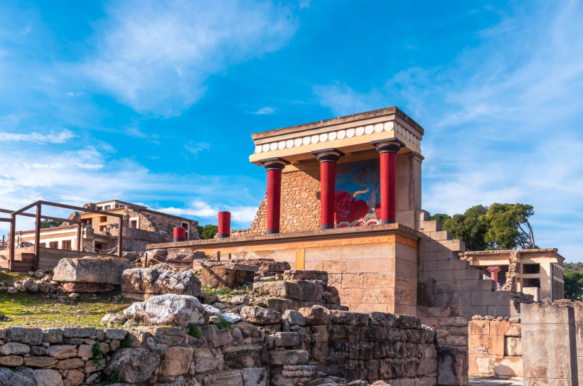 Rekonstruktion im Palast von Knossos mit roten Säulen und Fresko über den Ruinen unter blauem Himmel