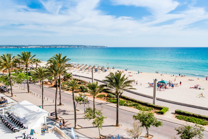 Strandpromenade und Sandstrand in El Arenal mit Palmen, Sonnenschirmen und Blick auf das Meer