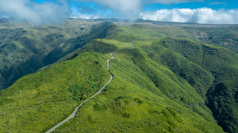 Luftaufnahme der Hochebene Paul da Serra auf Madeira mit kurviger Straße durch grüne Hügel und Wolkenlandschaft