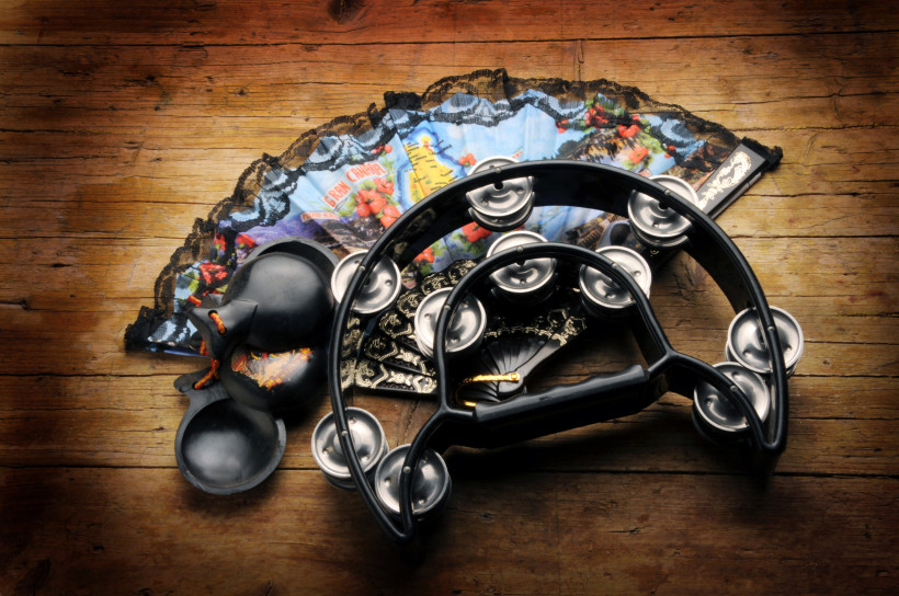 Lanzarote Traditionelle spanische Musikinstrumente und Accessoires auf einem Holztisch: Kastagnetten, Tamburin und zwei verzierte Fächer mit Spitzenrand und bunten Motiven.