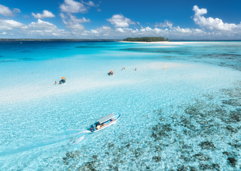 Sansibar - Mnemba Island  Türkisblaues, flaches Wasser an einer Sandbank vor Sansibar; Badende im seichten Meer und ein kleines Boot mit Sonnendach.