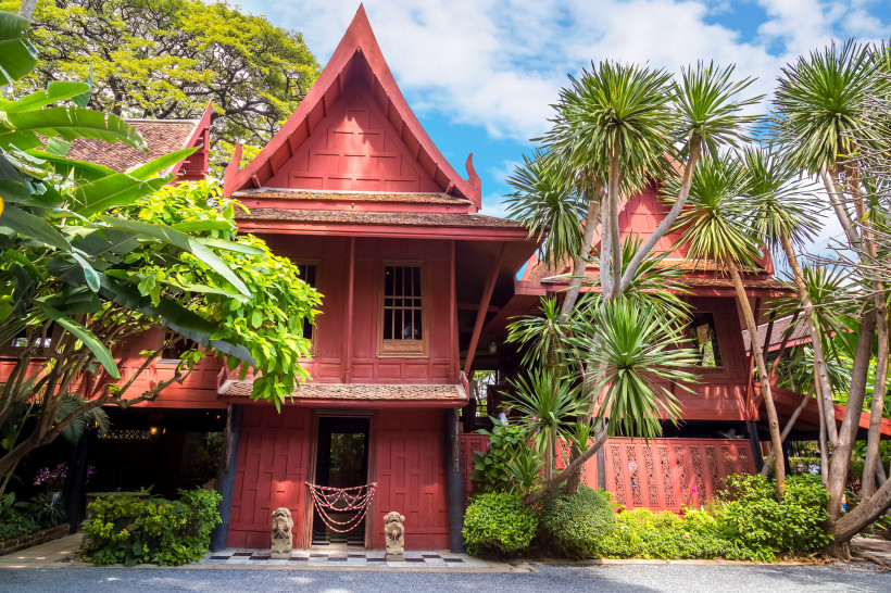 Traditionelles Jim Thompson House in Bangkok – Thailändische Architektur inmitten tropischer Gärten Rotes Jim Thompson House in Bangkok, umgeben von tropischen Pflanzen und traditioneller thailändischer Architektur