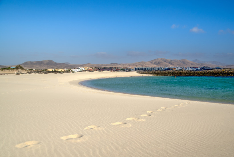 Sandstrand mit ruhiger Lagune, Fußspuren im Sand und Blick auf die Küste von La Concha bei Los Lagos