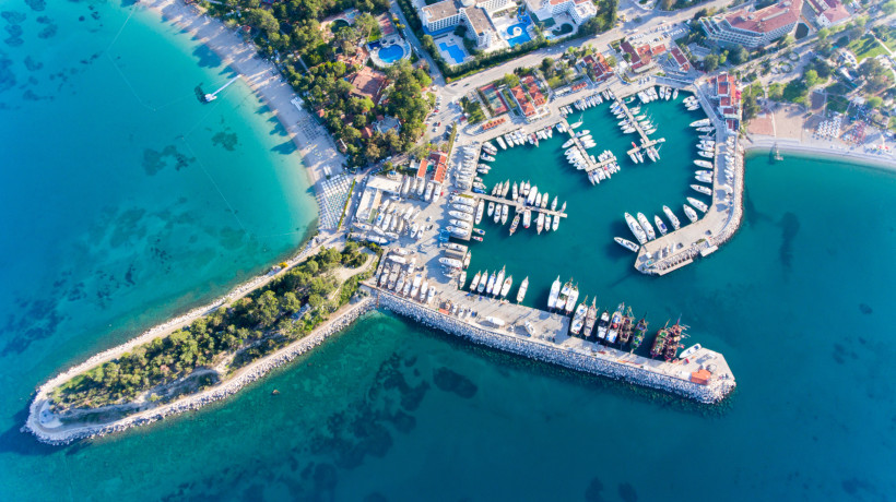 Drohnenaufnahme eines Yachthafens an der Türkischen Riviera mit Booten, Sandstränden, Hotels und kristallklarem, türkisfarbenem Meer