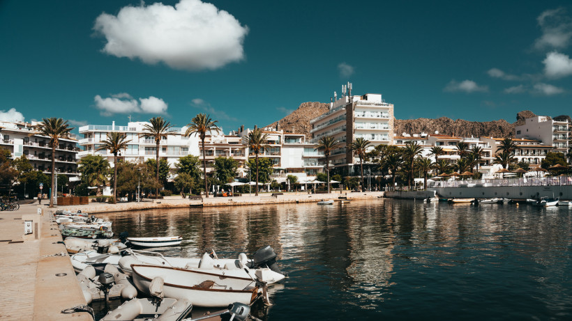 Hafen von Port de Pollença mit kleinen Booten im Vordergrund, Uferpromenade mit Hotels und Palmen