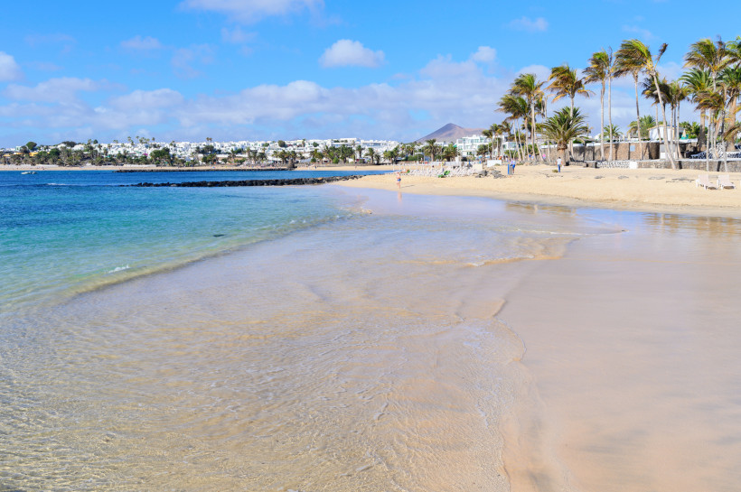 Costa Teguise Strand Lanzarote – feiner Sand, klares Wasser Feiner Sandstrand in Costa Teguise auf Lanzarote mit klarem türkisfarbenem Wasser, Palmen und Blick auf die Küstenbebauung
