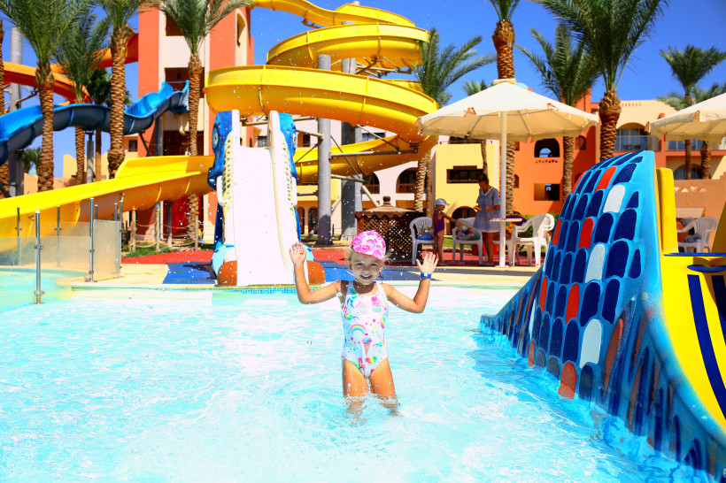 Ein Mädchen in Badeanzug und rosa Mütze spielt an einem heißen, sonnigen Tag in einem Badehaus. Schwimmen für Kinder. Ausgezeichnete Bedingungen für einen Familienurlaub. Aktive Erholung am Meer.