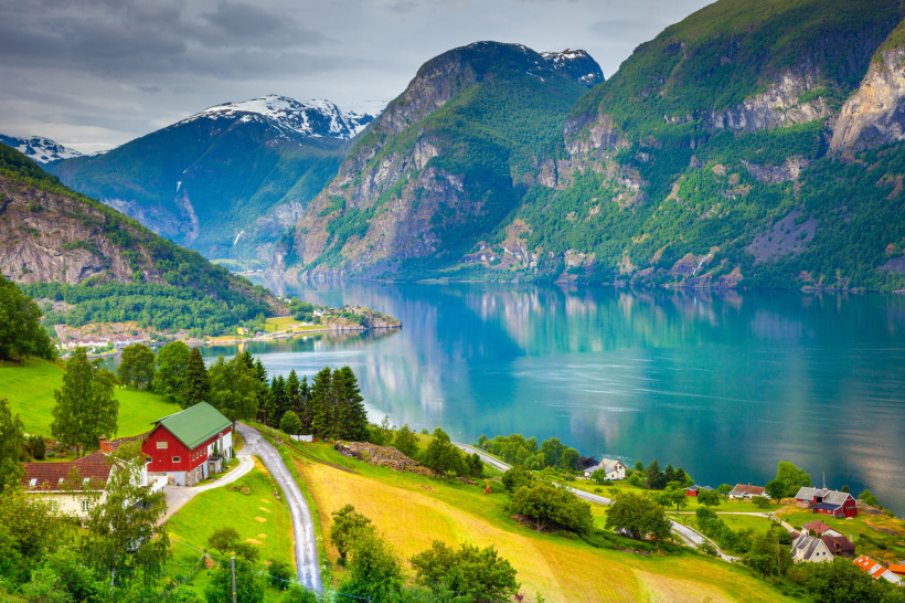 Blick auf den Sognefjord mit ruhigem Wasser, grünen Hängen und schneebedeckten Bergen im Hintergrund