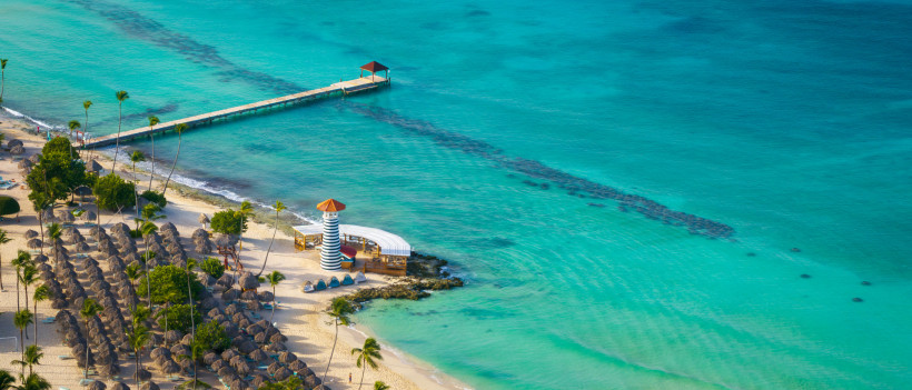 Küstenansicht in der Dominikanischen Republik mit Strand, türkisfarbenem Meer, Steg und kleinem Leuchtturm
