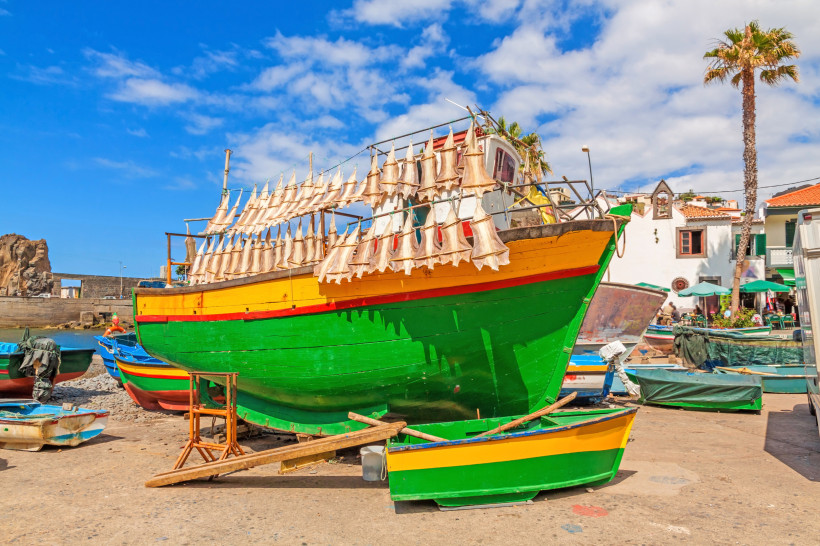 Buntes Fischerboot mit aufgehängtem Trockenfisch in Câmara de Lobos auf Madeira bei blauem Himmel