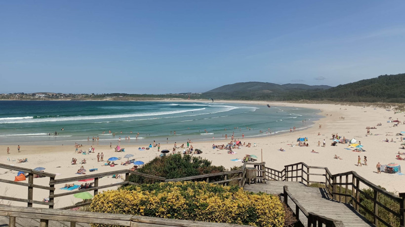 Blick auf den Strand von San Xurxo mit Sandfläche, Badegästen, Wellen und Holzsteg im Vordergrund