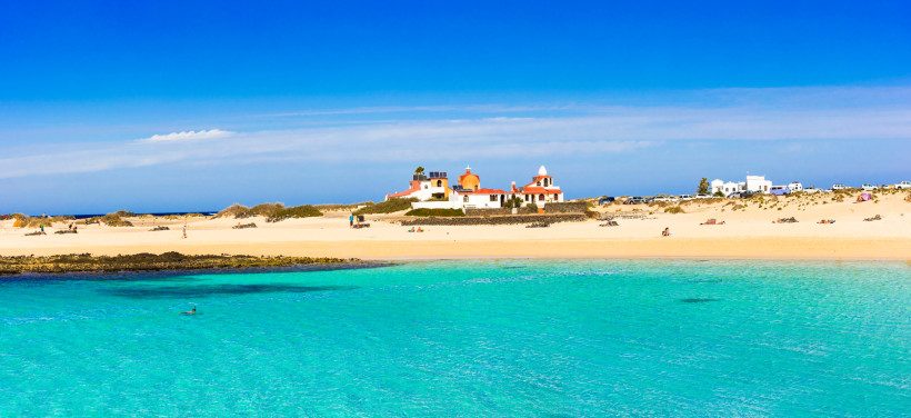 Strand und türkisfarbenes Meer bei El Cotillo mit weißer Kirche im Hintergrund