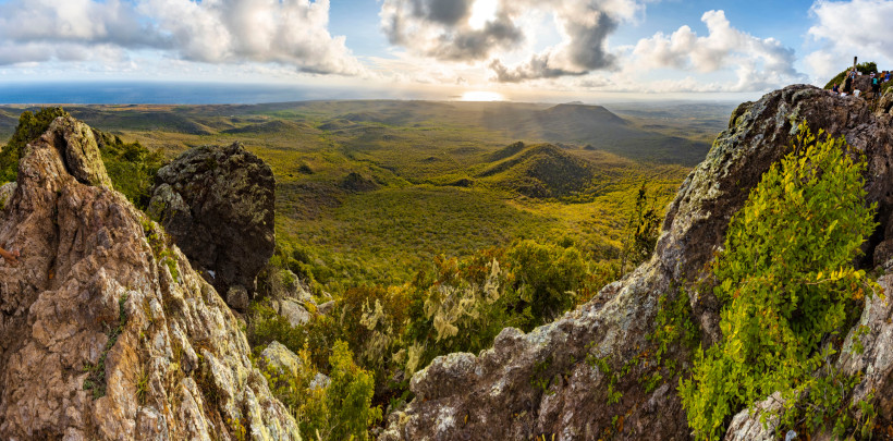 Curaçao Atemberaubender Ausblick vom Gipfel des Christoffelbergs auf Curaçao. Im Vordergrund sind große, zerklüftete Felsen zu sehen, die mit grünem Gestrüpp und Moos bewachsen sind. Dahinter breitet sich eine weite, grüne Hügellandschaft aus, die bis zum Horizon